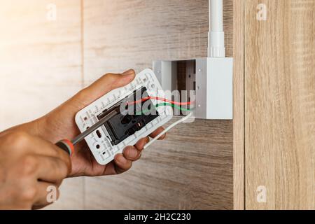 Hand of an electrician is using a screwdriver to attach the wires to the socket. Stock Photo