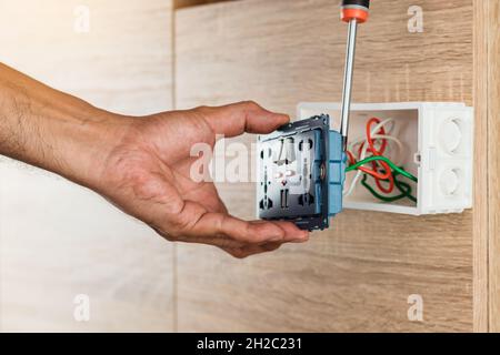 Hand of an electrician is using a screwdriver to attach the wires to the universal wall outlet AC power plug with USB port and on-off in a plastic box Stock Photo