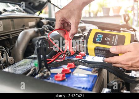 The car mechanic is using a voltage measuring instrument and charging the battery, the car's battery power. Stock Photo
