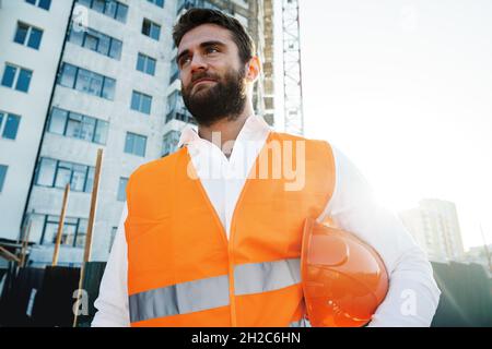 Builder wearing hardhat and safety vest standing on a commercial construction site Stock Photo