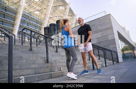 Full length shot of lovely sporty middle aged couple, man and woman in sportswear smiling while talking, standing together outdoors Stock Photo