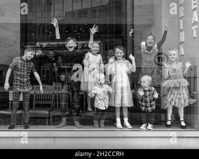 London, Greater London, England, October 09 2021: A group of children behind a window smile, wave and one does a robot dance. Monochrome image. Stock Photo