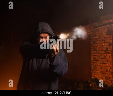 Caucasian man in a hood shoots a pistol Stock Photo - Alamy