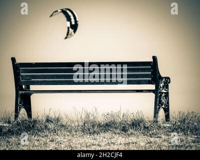 Kite flying by an empty bench by the sea Stock Photo