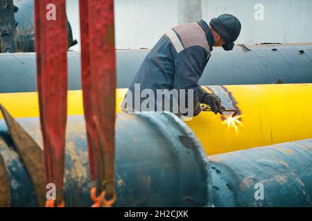 The welder cuts a large yellow pipe with acetylene welding for gasification. Disposal of old used metal pipes. Authentic workflow scene. Industrial background. Stock Photo