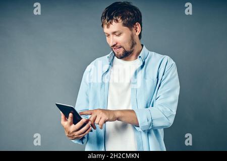 A middle-aged white Caucasian man holds a tablet in his hand and looks at a mobile application. A satisfied guy uses the Internet from a mobile device. Stock Photo