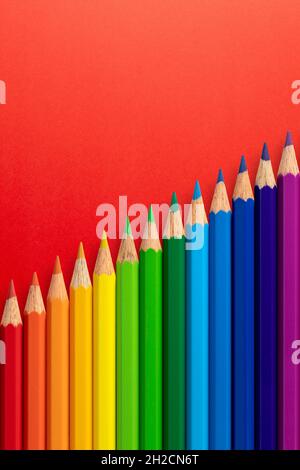 Colour pencils arranged diagonally on a red vertical paper background. Stock Photo