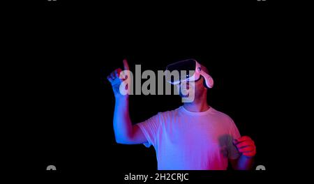 Young man using vr glasses in black background and neon light environment. Stock Photo