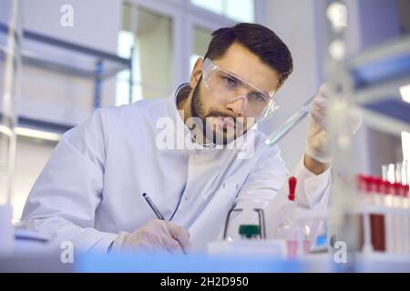 Male scientist looks at a test tube with liquid in his hand and records the results of the study. Stock Photo