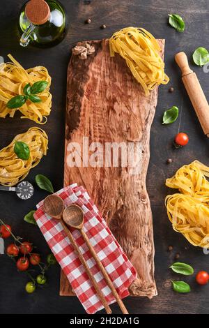 Tagliatelle. Homemade pasta, basil leaves, flour, pepper, olive oil, cherry tomato and rolling pin and pasta knife on dark old wooden background. Food Stock Photo