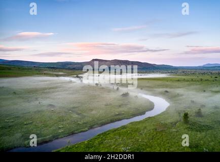 Majestic aerial scenery of curved river flowing along green valley in highlands on foggy morning in Iceland
