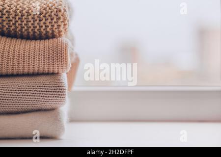 A stack of warm knitted sweaters on the windowsill in pastel shades. Stock Photo