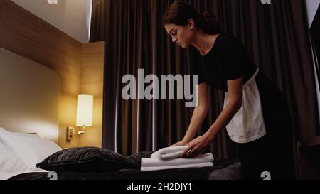 young chambermaid putting fresh white towels on bed in hotel room Stock Photo