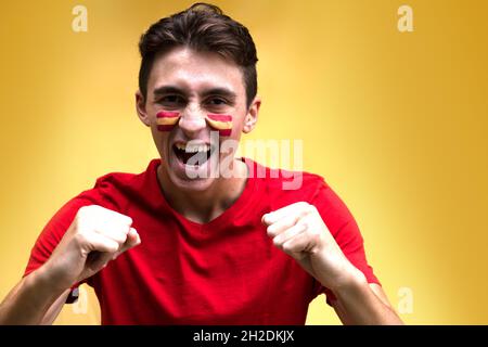 Spanish football fan happy for his national team, isolated on yellow background. Flag painted over face Stock Photo