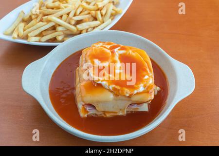 Francesinha is a Portuguese sandwich, made with bread, ham, linguica, sausage, steak, and covered with, cheese and beer sauce. Close up Stock Photo