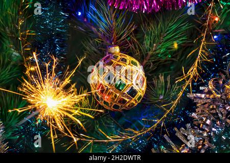 Christmas New Year background. A multi-colored ball on a Christmas tree and a burning sparkler. Christmas tree decoration with a shiny ball and sparkl Stock Photo