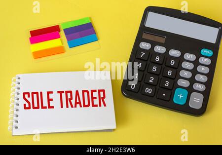 Top view of calculator, sticker and notepad with phrase SOLE TRADER isolated on yellow background. Business concept. Stock Photo