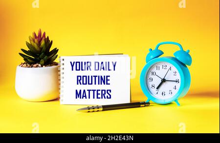 Your daily routine. Written on a notepad, next to an alarm clock, a cactus and a pen on a yellow background Stock Photo