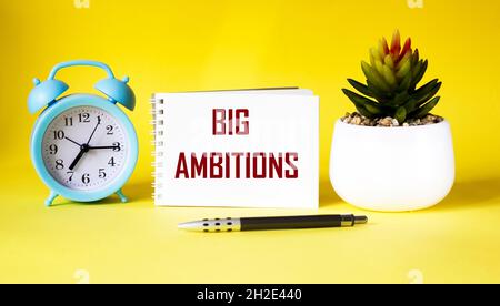 text BIG AMBITIONS on notepad and yellow background. Stock Photo