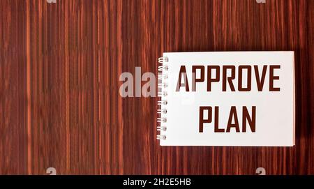 Approved plan. The text APPROVED PLAN is written in a notebook on a wooden background. Stock Photo