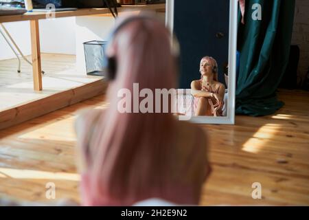 Reflection of thoughtful woman with color hair listening to music in front of mirror Stock Photo