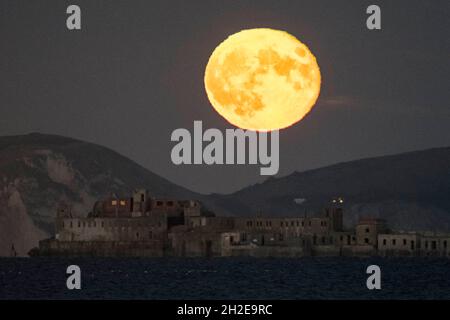 Portland, Dorset, UK.  21st October 2021.  UK Weather.  The almost full Hunter’s Moon rises up from behind the cliffs of the Jurassic Coast above the historic 19th century Portland Breakwater Fort on the outer breakwater of Portland Harbour near Weymouth in Dorset.  The now derelict fort also known as Chequered Fort was constructed between 1868 and 1878 and is Grade II listed.  Picture Credit: Graham Hunt/Alamy Live News Stock Photo