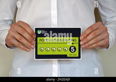 Restaurant manager holds a sticker with Food Hygiene rating 5 from The United Kingdom Food Standards Agency Stock Photo