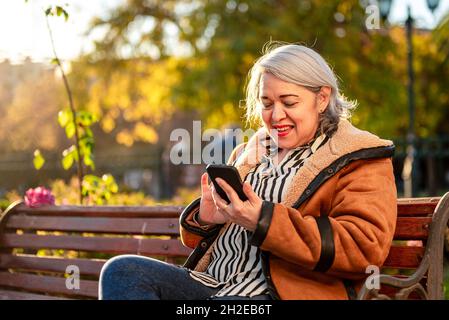 Mature woman using smart phone outdoor at the park Stock Photo