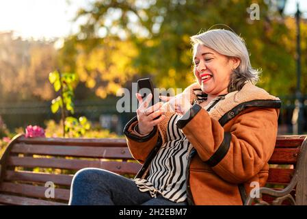Mature woman using smart phone outdoor at the park Stock Photo