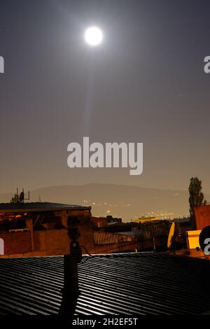 Full moon at the middle of the night in Bursa, Moon and light reflection on the metal roof in ghettos in bursa with uludag and city light background Stock Photo
