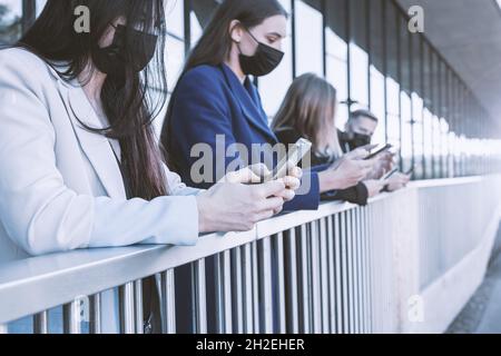 Business, social distancing, covid-19 concept. Young people with face masks using cell phones in urban area background. Closest womans hands is in foc Stock Photo
