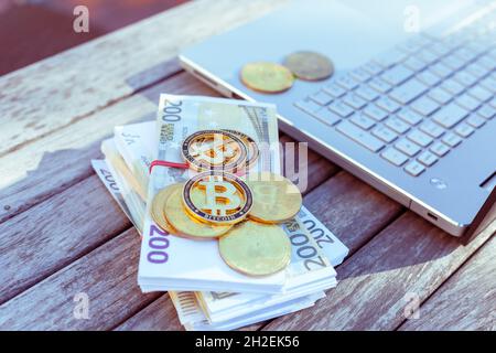 There are bitcoins money and a laptop on the table. Bitcoin coins lie on paper euros. Stock Photo