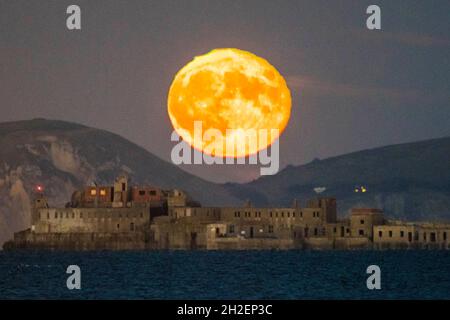 Portland, Dorset, UK.  21st October 2021.  UK Weather.  The almost full Hunter’s Moon rises up from behind the cliffs of the Jurassic Coast above the historic 19th century Portland Breakwater Fort on the outer breakwater of Portland Harbour near Weymouth in Dorset.  The now derelict fort also known as Chequered Fort was constructed between 1868 and 1878 and is Grade II listed.  Picture Credit: Graham Hunt/Alamy Live News Stock Photo