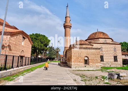 Cobblestone walking path between islamic art museum in iznik and seyh kutbuddin, son tomb made of red bricks wall with walking women yellow wearing. Stock Photo