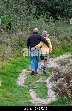 older middle-aged couple walking arm-in-arm together along a countryside pathway or track, older lovers walking with each other, older couple in love Stock Photo