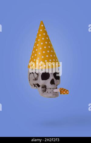 Human skull  with a yellow birthday cap and whistle  isolated on a purple background. Minimal holiday celebration funny concept Stock Photo