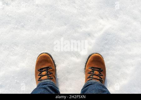 Closeup top above view of male legs in jeans and brown leather warm boots isolated on white icy snow surface background. Detail waterproof shoes Stock Photo