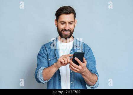 Smiling man using smartphone standing isolated on blue background copy space Stock Photo