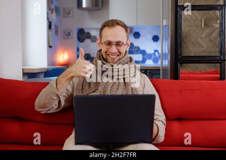 Middle age man using laptop at sofa happy with big smile doing ok sign, thumb up with fingers, excellent sign. Stock Photo