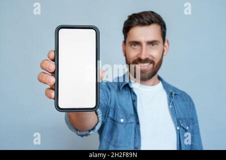 Satisfied smiling man showing mobile phone blank white screen mockup to camera Stock Photo
