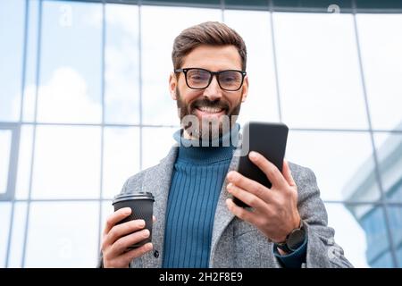 Laughing businessman watching funny video drinking coffee outside office Stock Photo