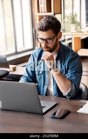 Handsome focused man working using laptop sitting at office desk table Stock Photo