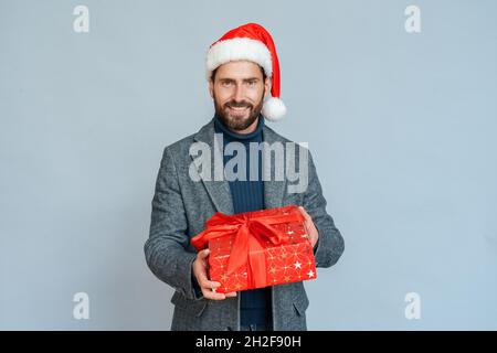 Successful businessman in formal suit and Santa hat giving gift box on blue Stock Photo