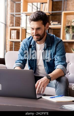 Smiling man working on laptop, checking email, writing message in social network Stock Photo