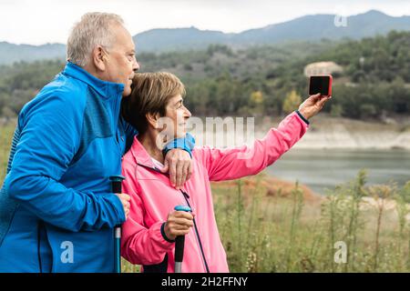 Happy senior couple having fun taking a selfie hiking in the woods - Focus on woman face Stock Photo