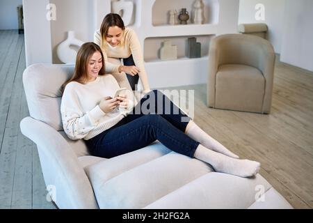 Two women on chaise longue with phone in lounge. Stock Photo