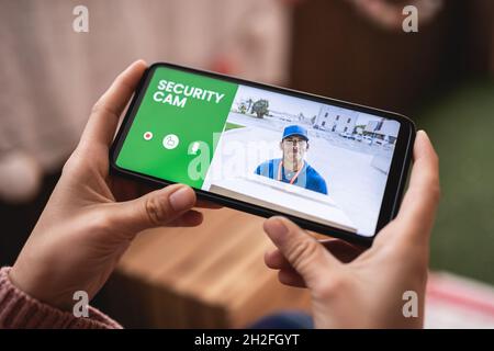 Woman watching delivery man through security camera system on mobile phone at home - Cctv smart technology lifestyle concept Stock Photo