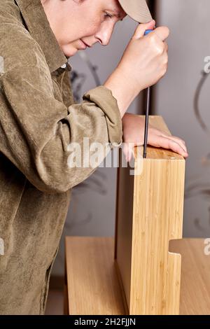 Assembler is tightening screws on drawer of flat pack furniture with screwdriver. Stock Photo