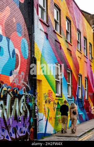 People Walk Past Buildings Covered In Colourful Graffiti, Shoreditch, London, UK. Stock Photo