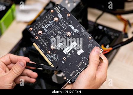 male hand holding and removes protective elastic band from PCI-E connector of video card. Backplate view of grafic card. Russia, 17.08.2021 Stock Photo